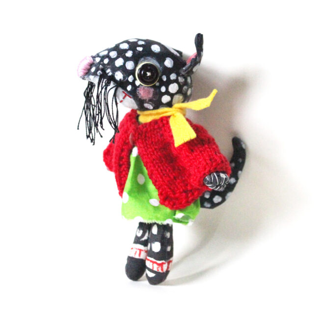 Ava is a a hand painted anthropomorphic quoll. She wears a green polka dot dress and hand knitted tiny red cardigan.