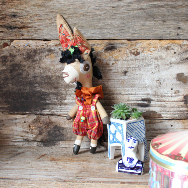 Emmett is a calico donkey, her wears silk red and yellow checked tartan pants and a orange ruffle.