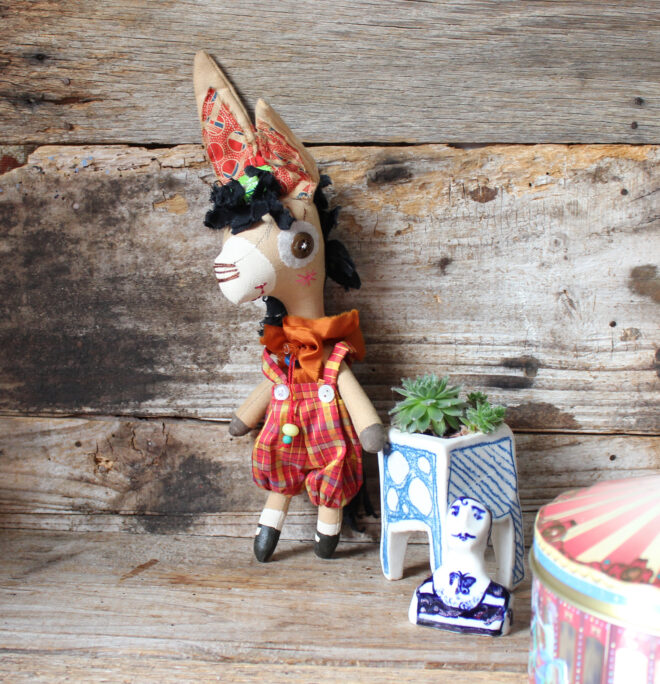 Emmett is a calico donkey, her wears silk red and yellow checked tartan pants and a orange ruffle.