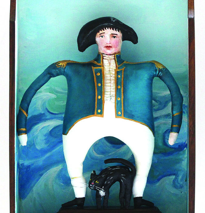 Mathew Flinders, in uniform, with his black cat, Trim. Painted fabric sculpture inside a wood drawer with waves painted in the background.
