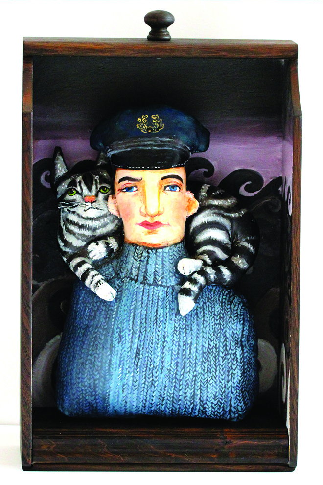 Harry McNish, dressed in a jumper and sailor cap, with his cat Mrs Chippy, on his shoulders. Fabric painted sculptures, inside a wood drawer. Rough sea waves are painted in the background.