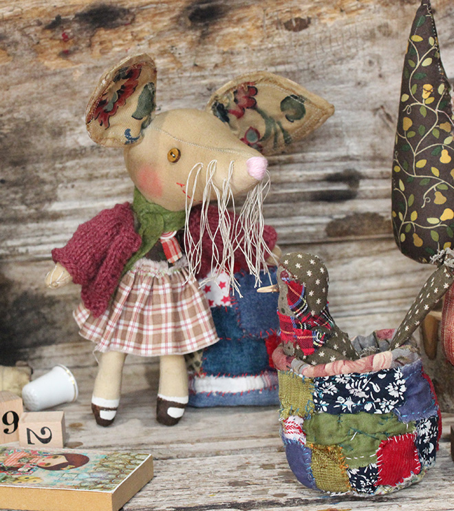 A small calico doll of a anthropomorphic Bilby. She is wearing a brown tartan dress and burgundy cardigan