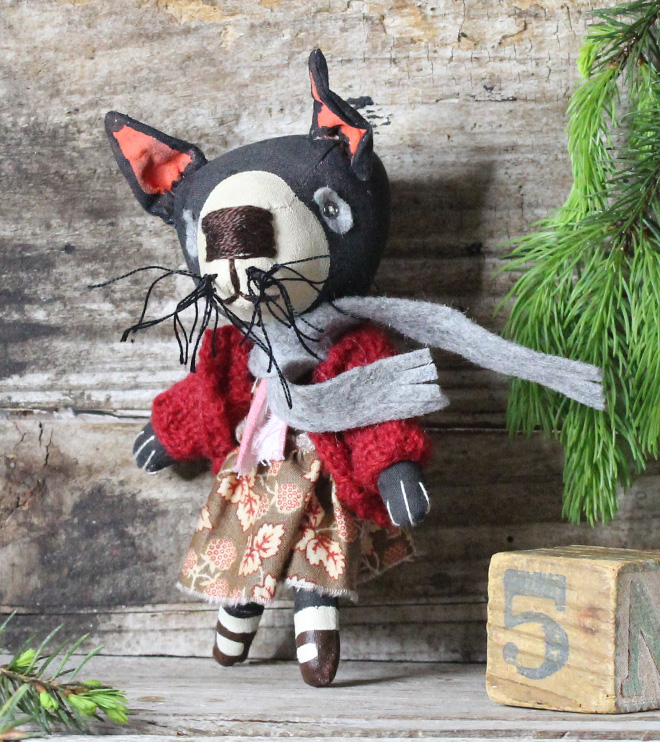Small handmade fabric Tasmanian devil doll, dressed in a red cardigan and brown dress. She has a grey wool scarf.